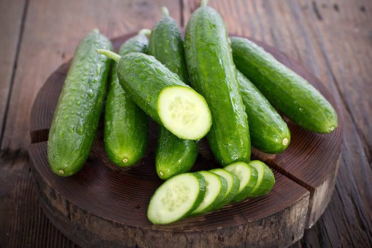 full and sliced cucumbers sitting on a round wooden cutting board