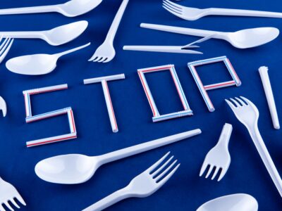 The word stop made of plastic tubes on a blue background with plastic utensils environmental pollution concept.