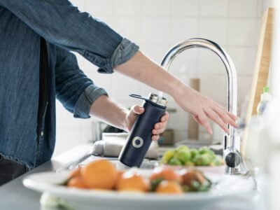 person filling stainless steel, reusable water bottle with kitchen faucet