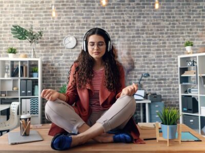 a woman sitting on a desk in a meditation pose with headphones on