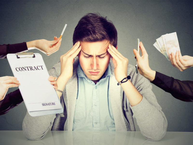 photo of stressed man holding his head with stressors surrounding him