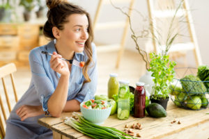 photo of a woman eating a salad, veggies and juice on table