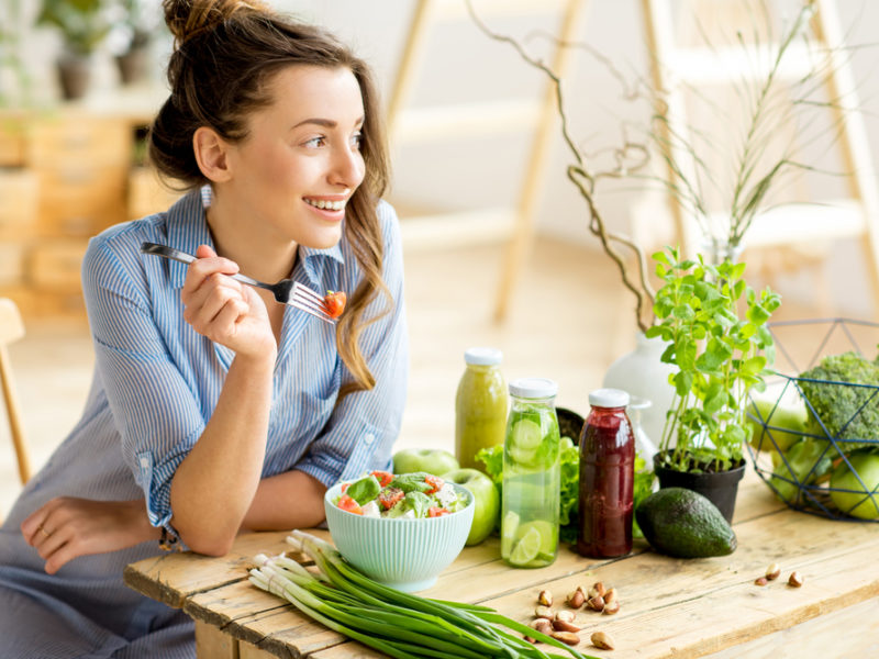 photo of a woman eating a salad, veggies and juice on table