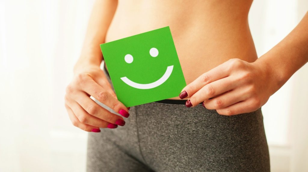 photo focused on midsection of woman, holding a green smiling face over her stomach