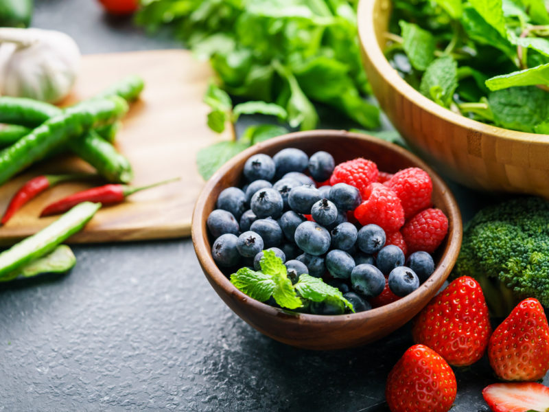 photo of bowl of berries, greens, and other health veggies spread over a surface