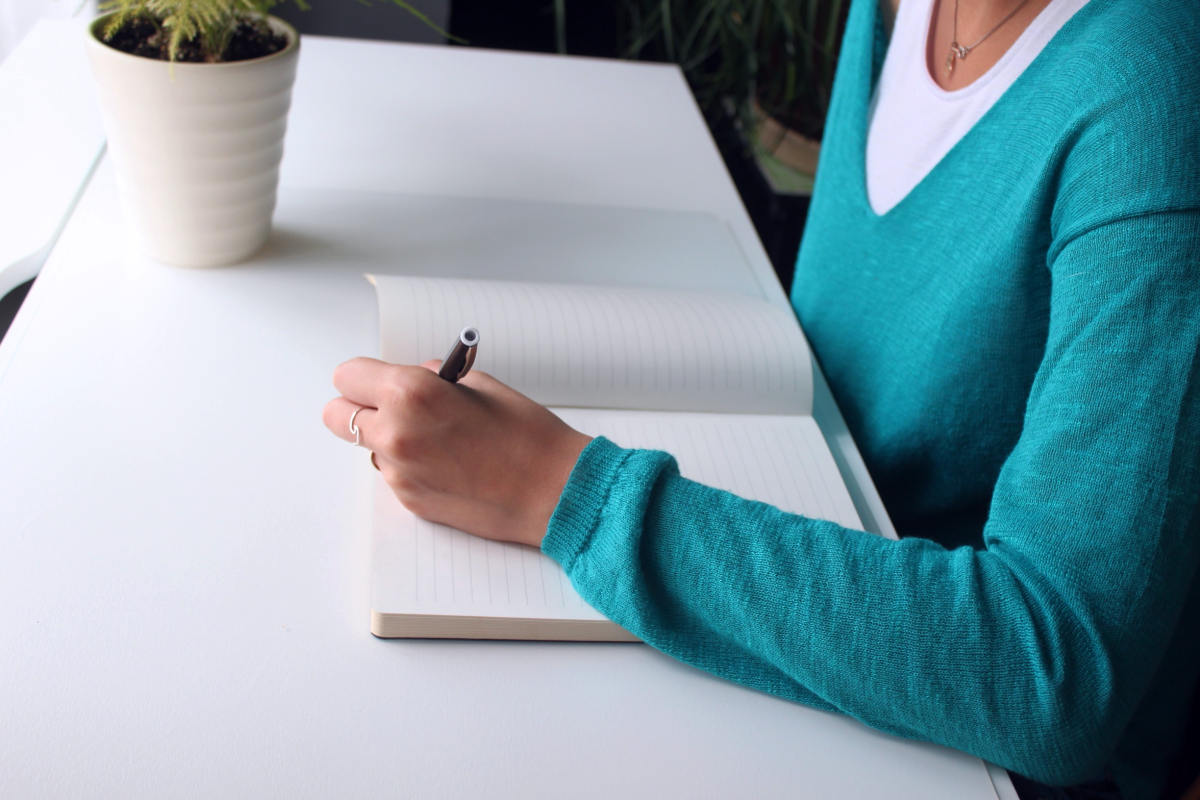 Woman writing on a notebook on a desk | 9 Sleep Tips Arianna Huffington Swears By