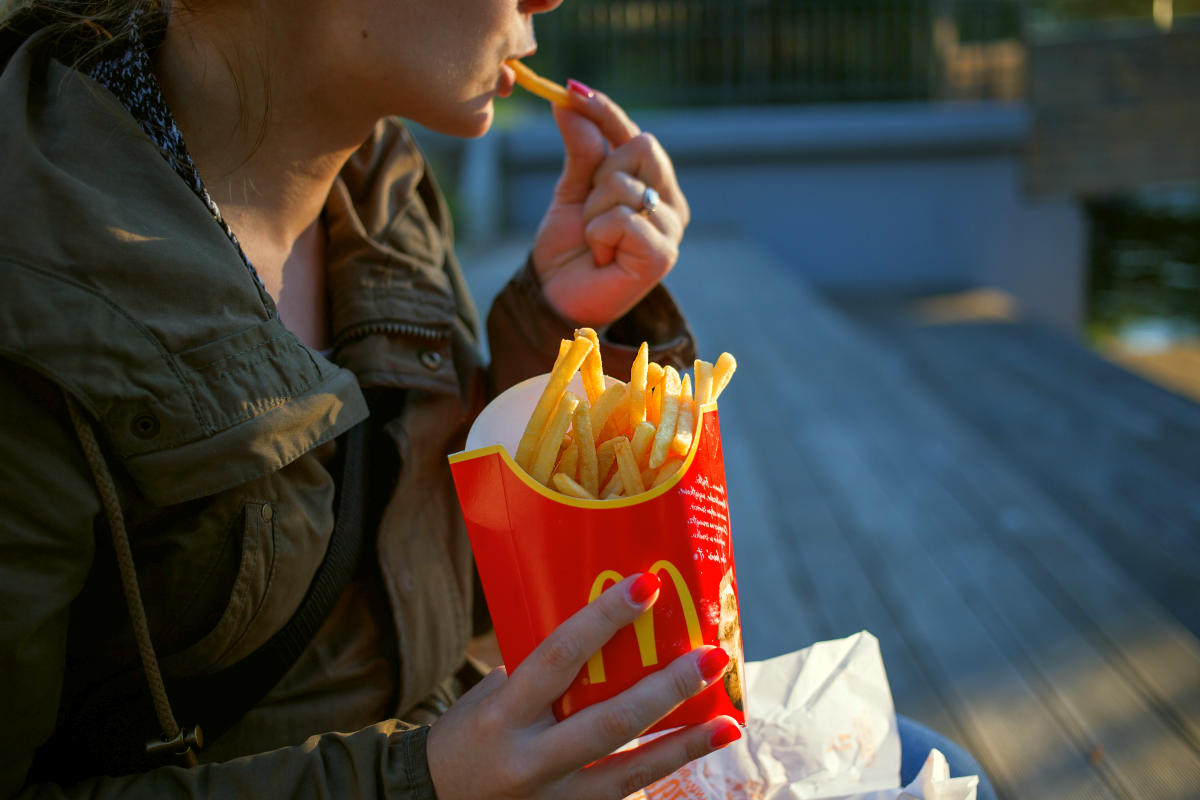 Woman in brown trench coat eating fries | Reasons To Stop Eating Processed Foods And 10 Healthy Swaps