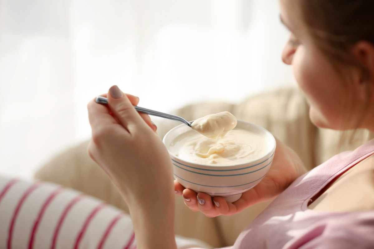 Bowl with yogurt and spoon in female hands | Foods To Add To Your Microbiome Diet