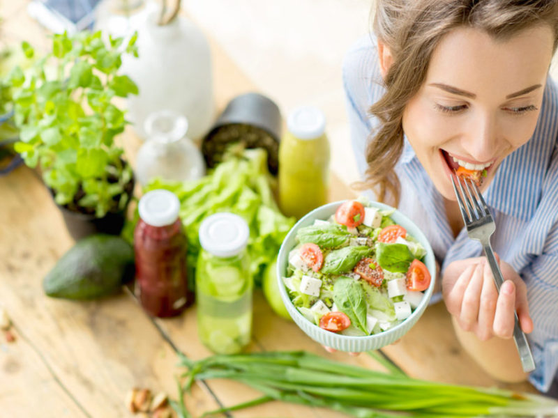 Photo of woman eating a salad with veggies and juices on the table