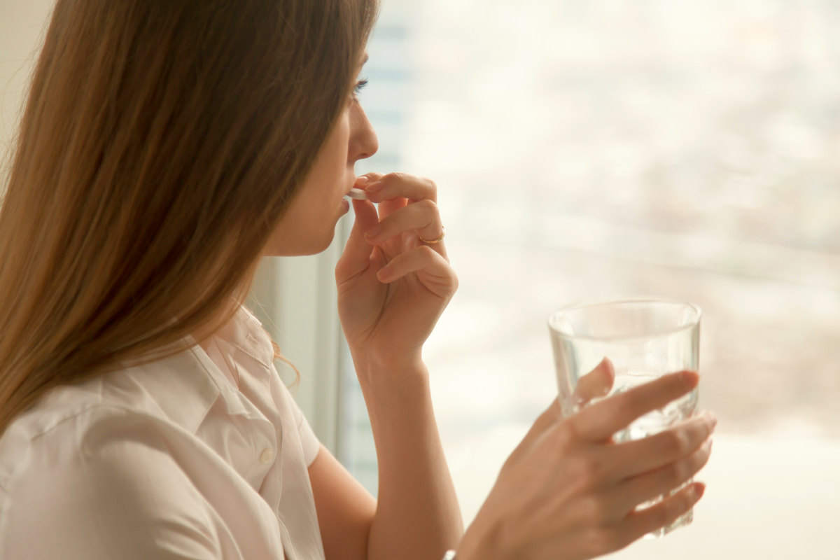 Young woman takes white round pill with glass of water in hand | Risks Of High TMAO And How To Reduce TMAO Levels