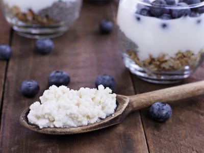 photo of kefir on a wooden spoon with kefir, blueberry, and granola parfaits in the background