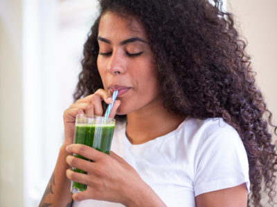 photo of young woman drinking a glass of green juice