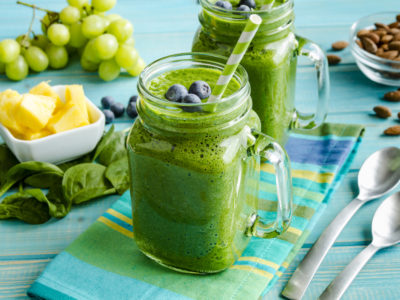 photo of a green smoothie on a table with fruit and almonds