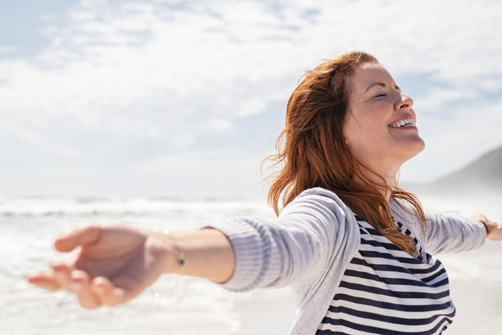 Happy,Redhead,Woman,Relaxing,With,Arms,Outstretched,At,Beach,With