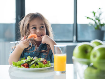 photo of a young girl eating salad and drinking juice