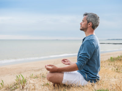 photo of man practicing mindfulness meditation on a beach