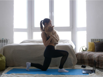woman working out at home on a yoga mat while holding her cat