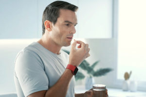 A man takes supplements in his kitchen