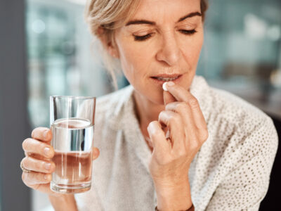 photo of mature woman holding a glass of water and taking probiotics for women