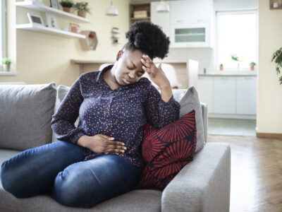 woman on couch holding head and stomach in pain caused by gut dysbiosis