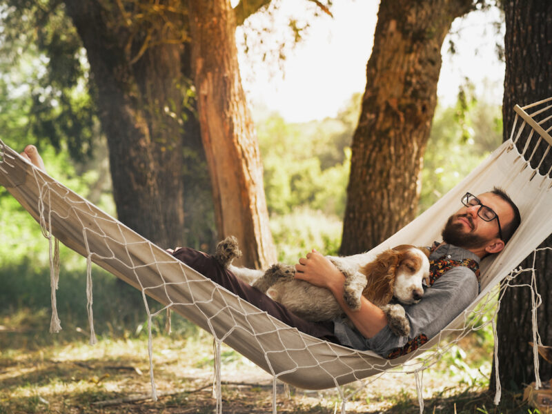 photo of man relaxing in hammock with dog for self-care