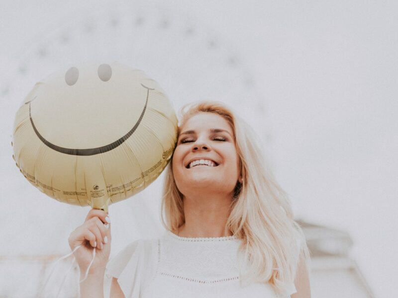photo of happy, smiling woman holding a smilie face balloon