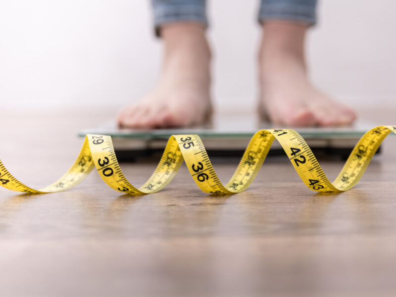 lose weight concept, photo of woman standing on scale with tape measure stretched out on the floor in foreground