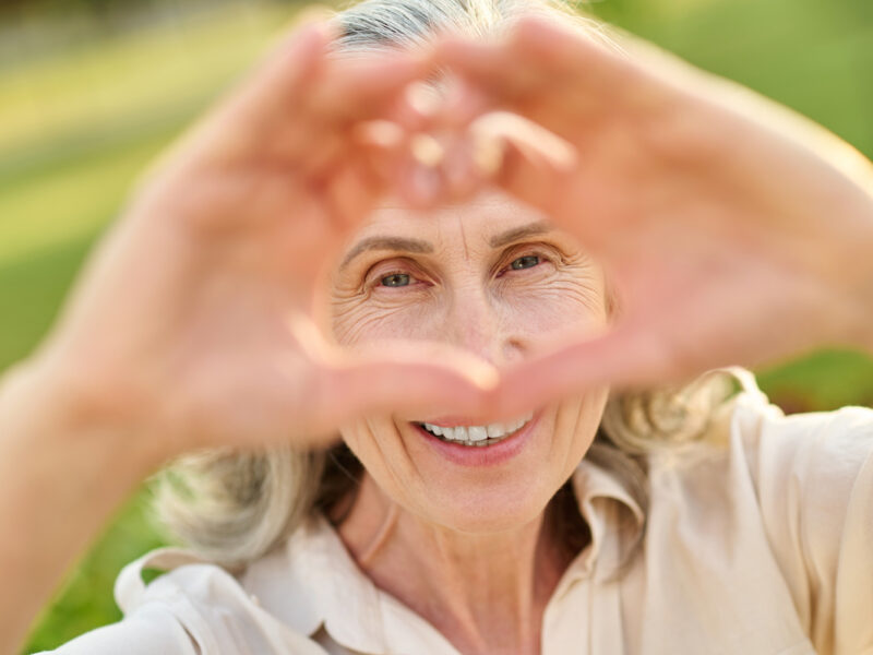 happy older woman looking through heart shape hands