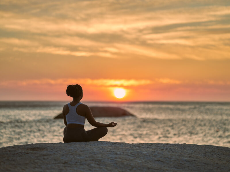 woman doing yoga (easy pose) on a beach at sunset