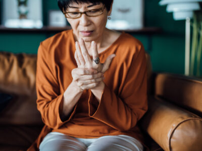 photo of senior Asian woman rubbing her hands in discomfort, suffering from joint pain from high uric acid