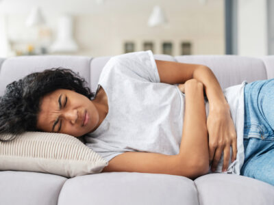 photo of young woman laying on couch holding stomach in pain from IBS symptoms