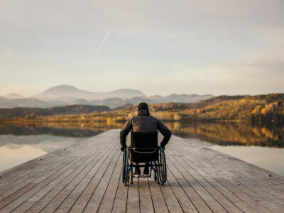 photo of man in wheelchair enjoying mountain view on pier