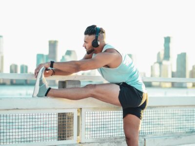 man wearing headphones, stretching after exercise in front of a cityscape
