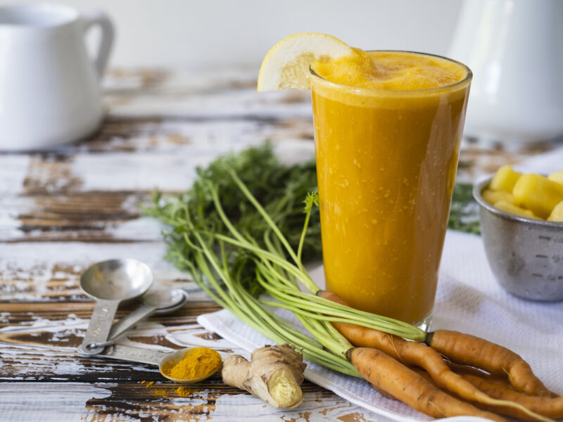 Carrot and ginger smoothie with pineapple and turmeric with ingredients on the side.