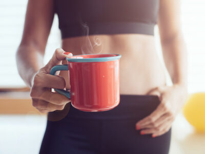 Athletic young woman with cup holding cup of coffee in front of abdomen
