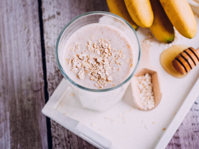 Delicious Healthy breakfast or snack. Chai tea, banana smoothie with oat flakes, and honey in glass on wooden table background. 