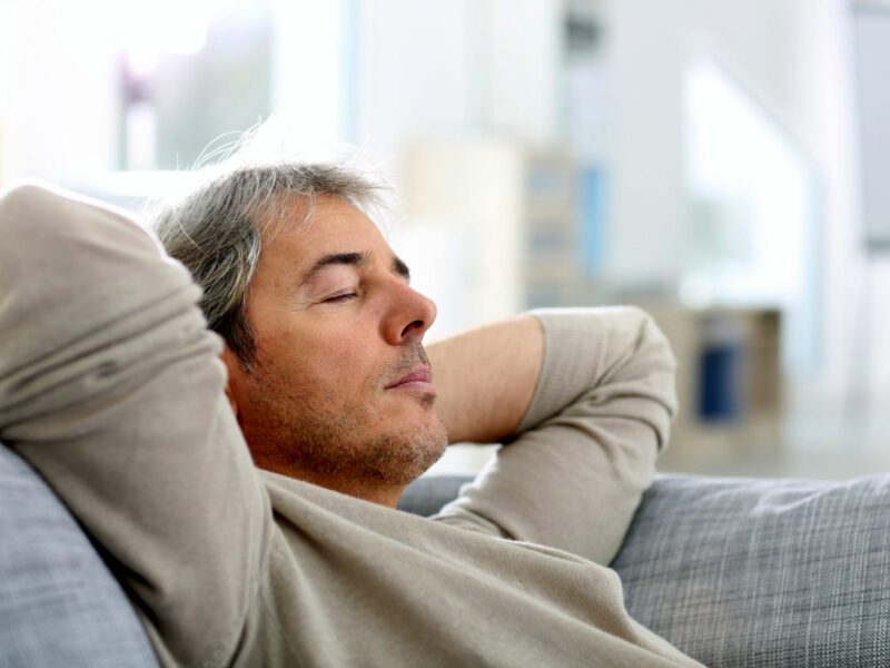 Man taking nap on sofa with arms behind head
