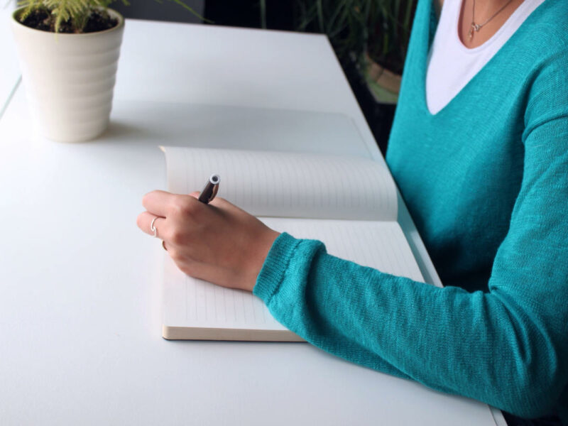 Woman writing in journal at white desk