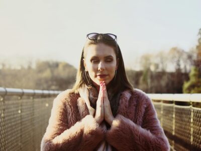 woman in brown fur coat wearing black framed eyeglasses on top of head and holding hands together in prayer pose, gratitude