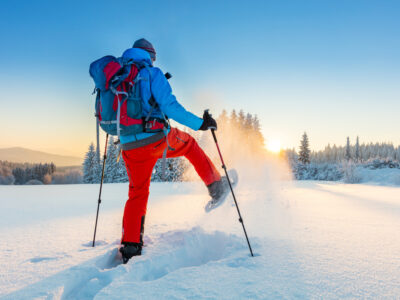 Snowshoe walker running in powder snow with beautiful sunrise light; fun winter activities that burn calories