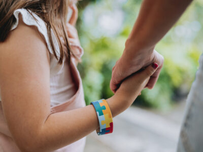 photo of parent holding hand of child with autism, wearing autism awareness bracelet