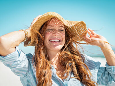 photo of woman standing in the summer sun smiling and holding the brim of her hat