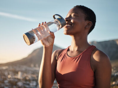 photo of young, healthy woman outdoors smiling and drinking mineral water