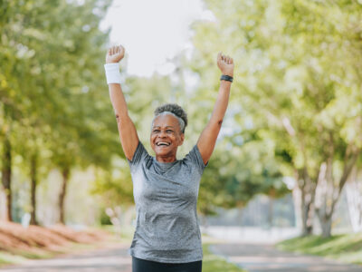 woman exercising outdoors, smiling with arms raised in air triumphantly