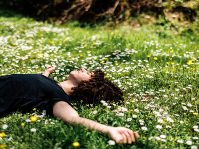 Photo of teenage boy laying in grass and flowers with arms outstretched