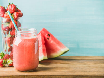 photo of watermelon summer smoothie for gut health with watermelon slices and strawberries in background