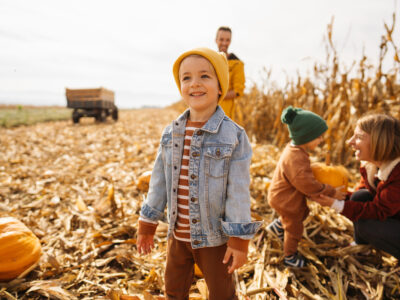 photo of happy family pumpkin picking with focus on young boy in fall clothing in the foreground