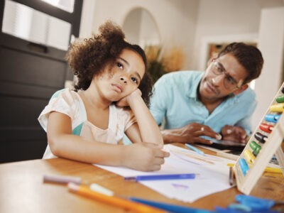 Worried Indian dad with sitting with distracted daughter who is working on homework at home; ADHD in girls and women concept