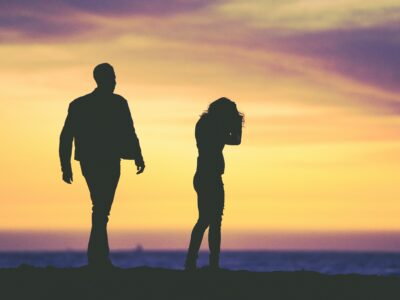 couple silhouetted against sunset sky with woman looking upset