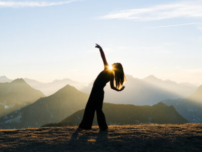 She is bending backwards as sun rises behind her. She is in an open meadow, Ticino Canton